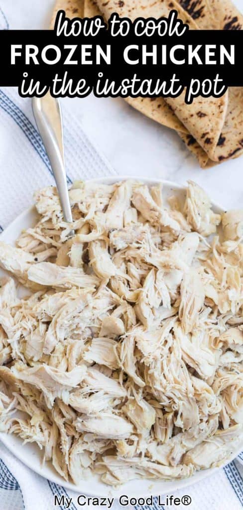close up of cooked shredded chicken in a white bowl with fork, wheat tortillas in the background. Text for Pinterest.