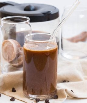 glass of iced coffee with mocha creamer ice cubes and coffee in the background