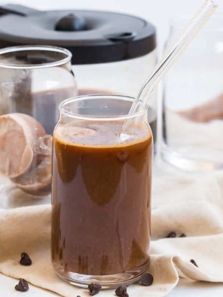glass of iced coffee with mocha creamer ice cubes and coffee in the background