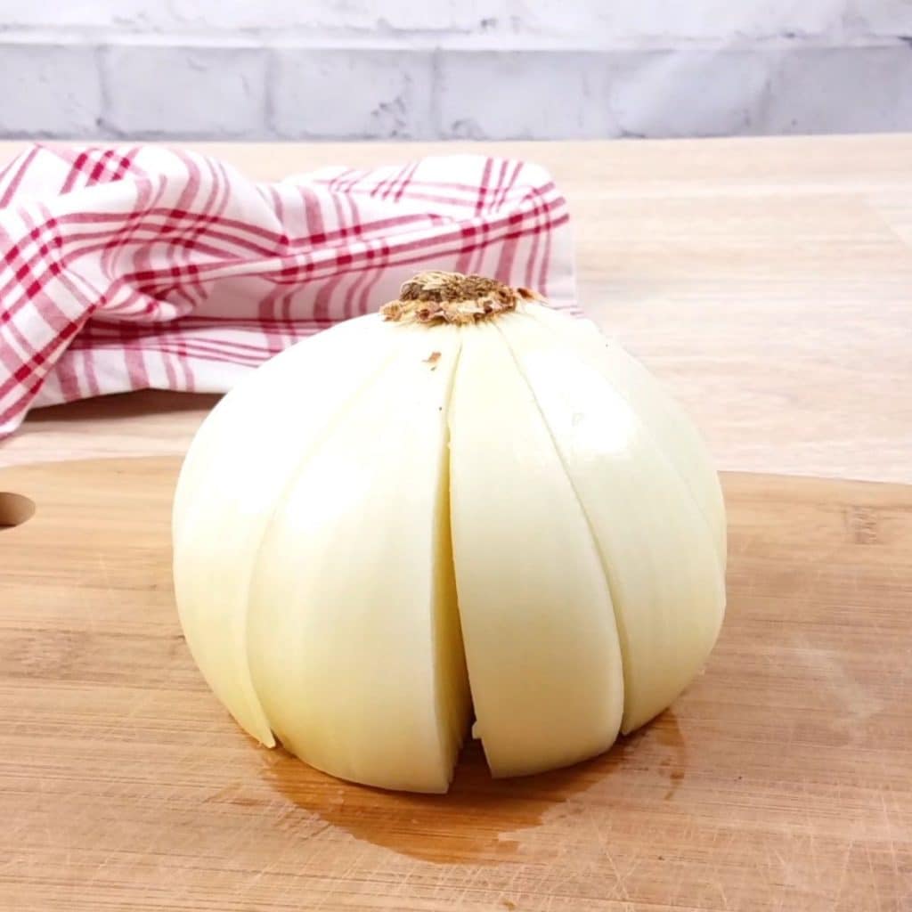 A peeled and partially cut  onion on a wooden cutting board.