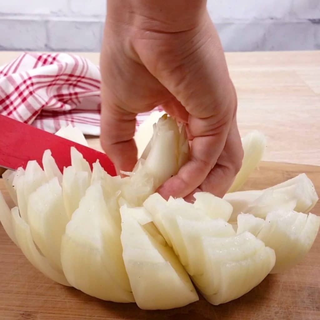 A red knife cutting an onion to form the petals of a blooming onion.