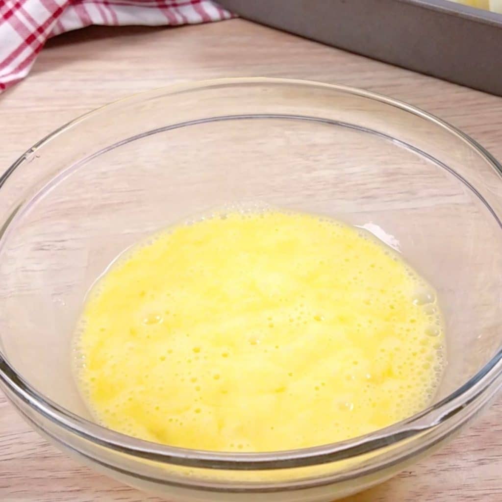 A glass bowl filled with whisked eggs.