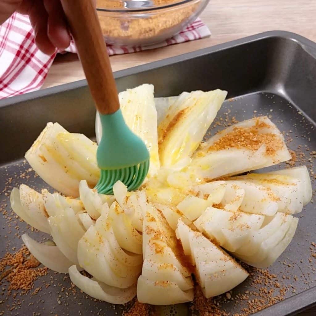 A sliced onion being brushed with an egg wash using a silicone basting brush.