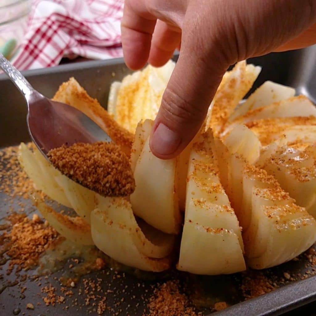 A cut onion being coated with seasoning using a spoon.