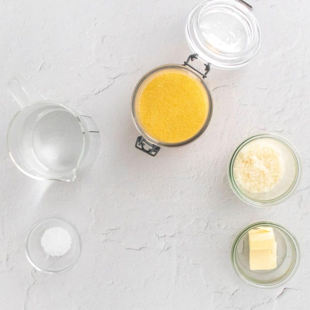 A white counter top with glass bowls and containers that have ingredients in them that are needed to make creamy polenta.