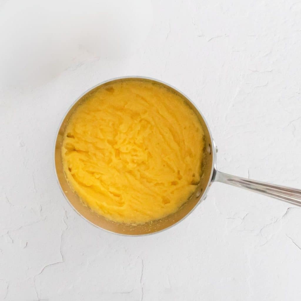 A white counter top that has a stainless steel saucepan with cooked polenta inside.