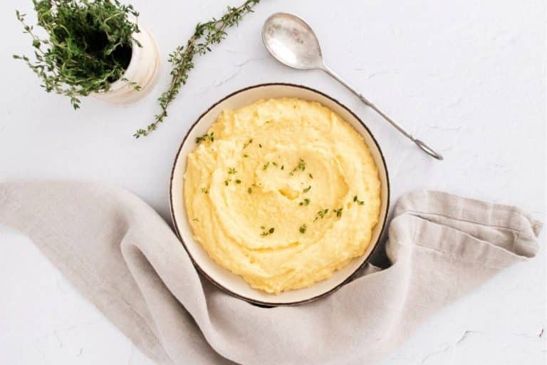 A neutral color counter and napkin with a bowl of creamy polenta with a sprinkle of thyme and off to the side is a cup of fresh thyme.