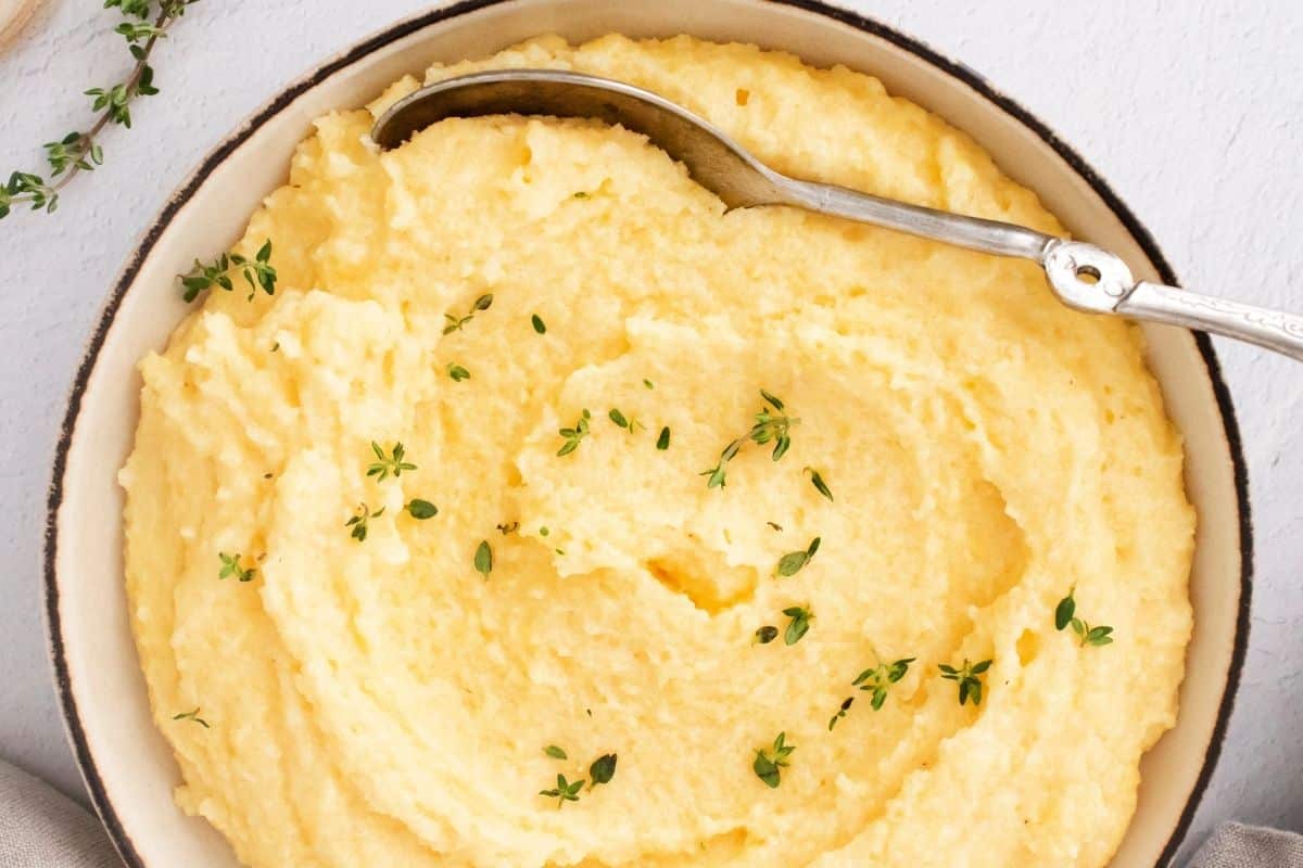 A close-up view of a bowl full of creamy polenta with a sprinkle of thyme and a spoon taking a scoop out.