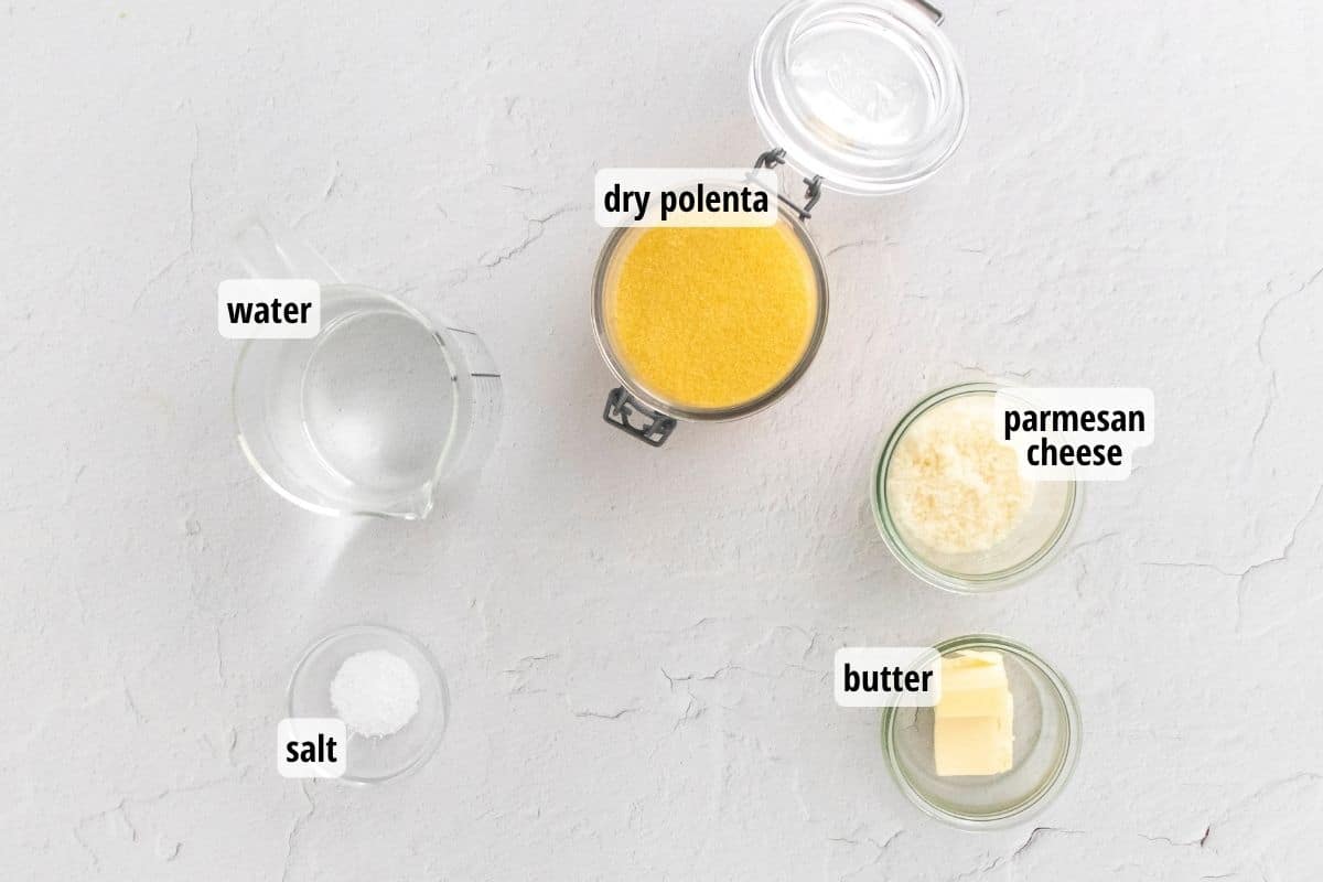 A white background with glass bowls and jars of labeled ingredients needed to make creamy polenta.