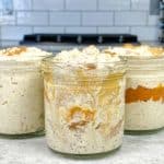 Several versions of pumpkin spice overnight oats on a countertop, including one with a pumpkin layer and one mixed with peanut butter.