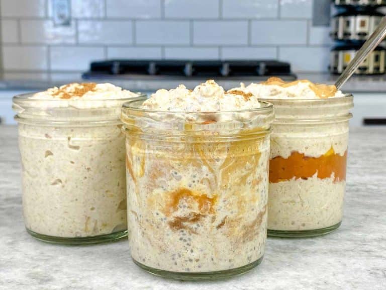 Several versions of pumpkin spice overnight oats on a countertop, including one with a pumpkin layer and one mixed with peanut butter.