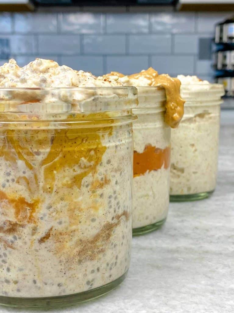 Three jars of Pumpkin Overnight Oats on a countertop. Each jar is made a little differently, but with basically the same ingredients.