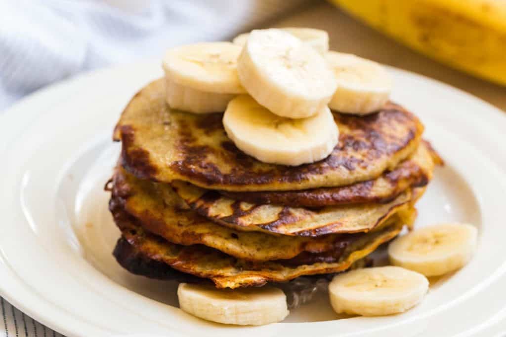 close up of a stack of banana pancakes topped with sliced bananas and syrup