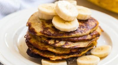 close up of a stack of banana pancakes topped with sliced bananas and syrup