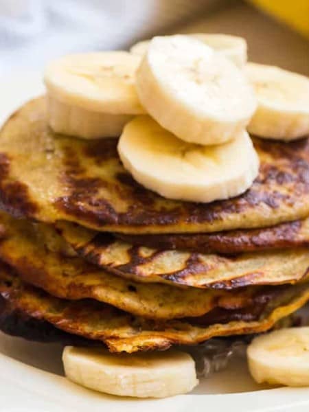 close up of a stack of banana pancakes topped with sliced bananas and syrup