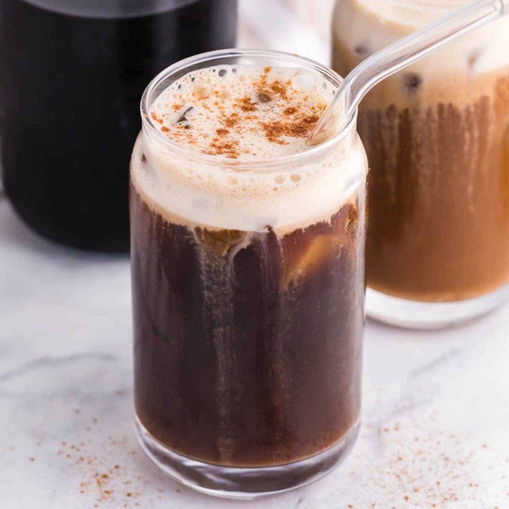 Carafe of French press coffee and two drinking glasses in front of it. The glasses have Pumpkin Cream Cold Brew with Cold Foam, sprinkled with cinnamon.