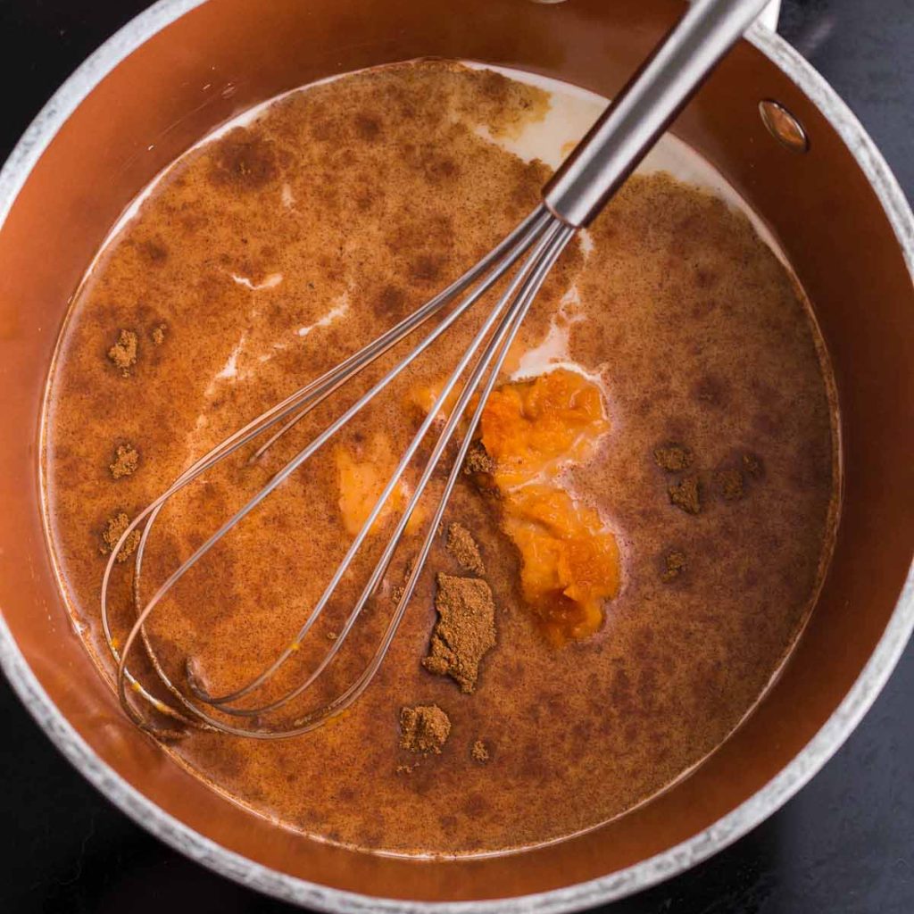 A pot on the stove with oat milk, spices, pumpkin, and vanilla being whisked together.