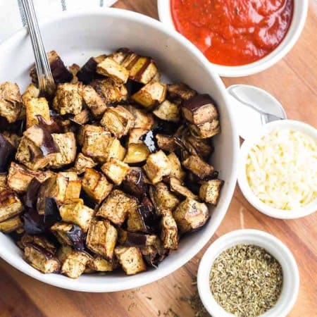 roasted eggplant cubes in bowl with seasoning and dipping sauce