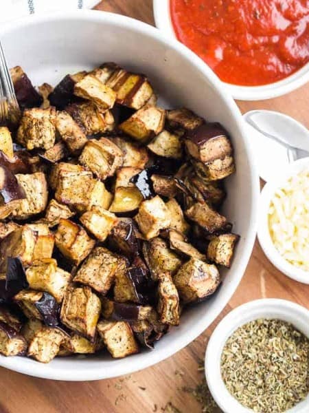 Roasted eggplant cubes in bowl with seasoning and dipping sauce.