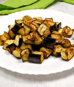 cooked eggplant on a white plate with a green linen