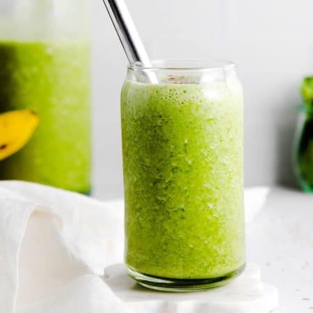 A glass cup filled with healthy green smoothie and has a metal straw.