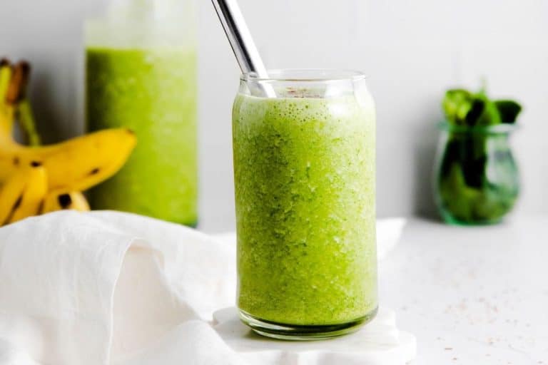 A glass cup filled with healthy green smoothie and has a metal straw.