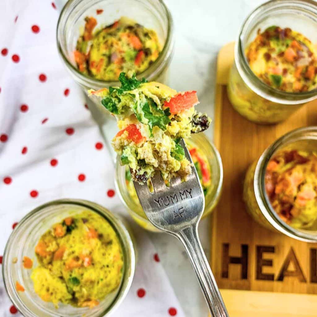 Six glass jars with cooked DIY Just Crack an Egg cups. There is a fork holding a bite up close to the camera.