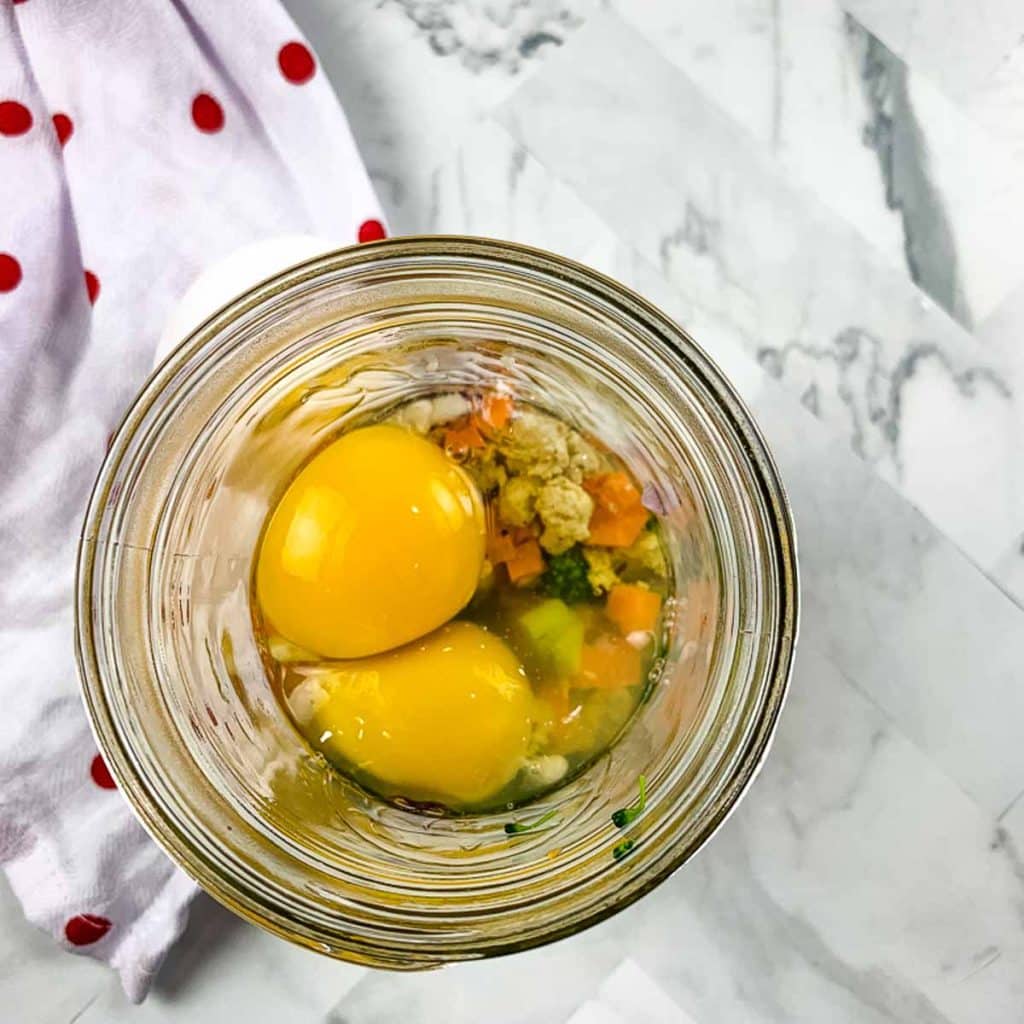 view from above of a mason jar with diced vegetables and topped with two eggs