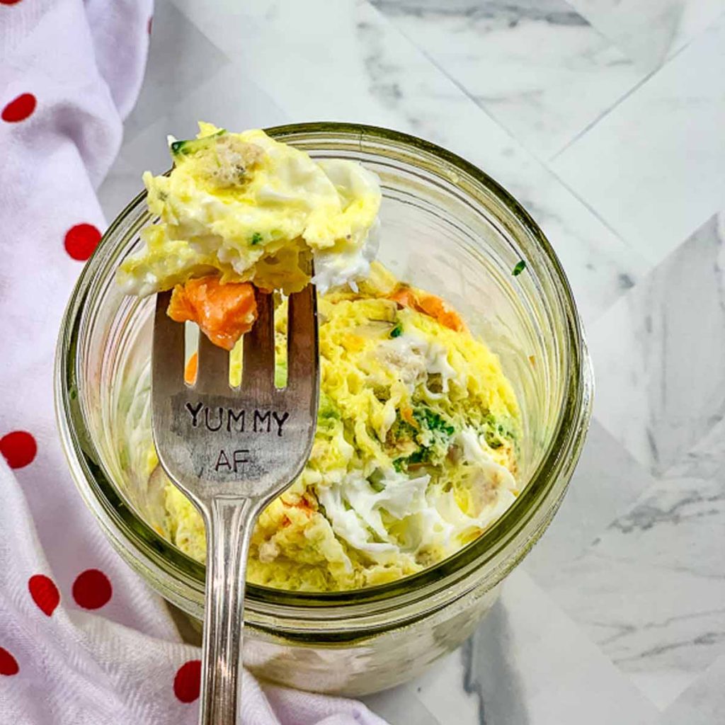 view from above of a mason jar with cooked egg and vegetables with a fork holding a bite of egg