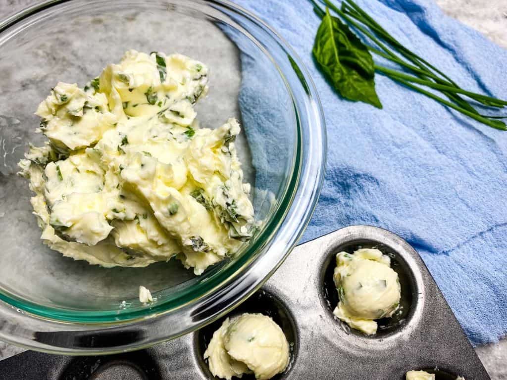 compound butter mix in a bowl next to fresh herbs and butter balls