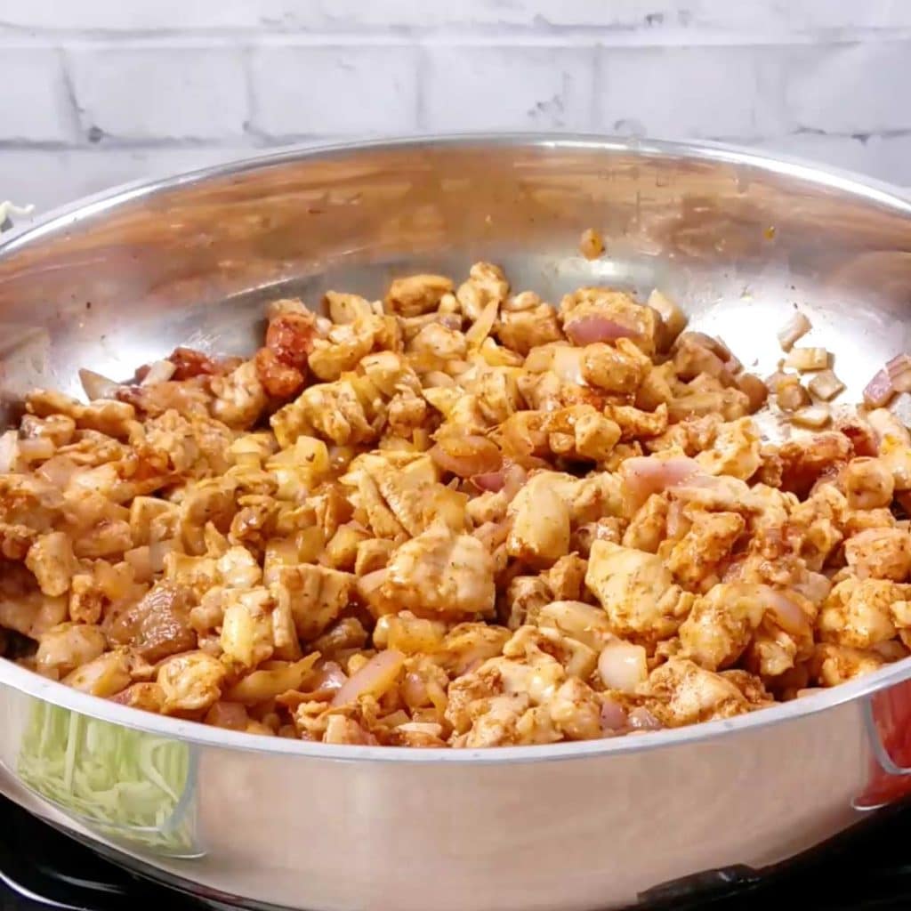 stainless steel pan with cooked chicken and diced onions and spices
