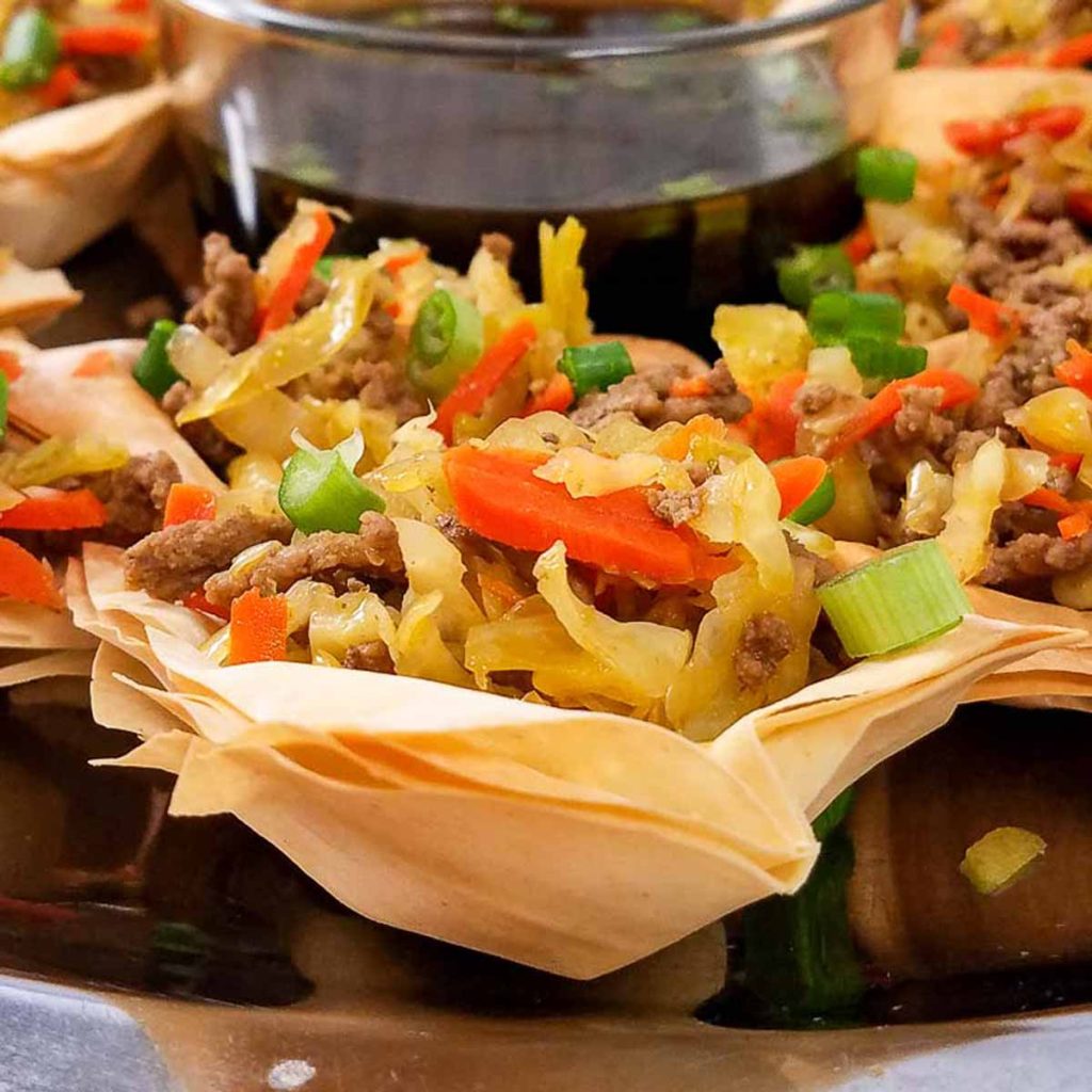 Deconstructed Egg Roll Wonton Cup on a platter with bowl of sauce in the background. 