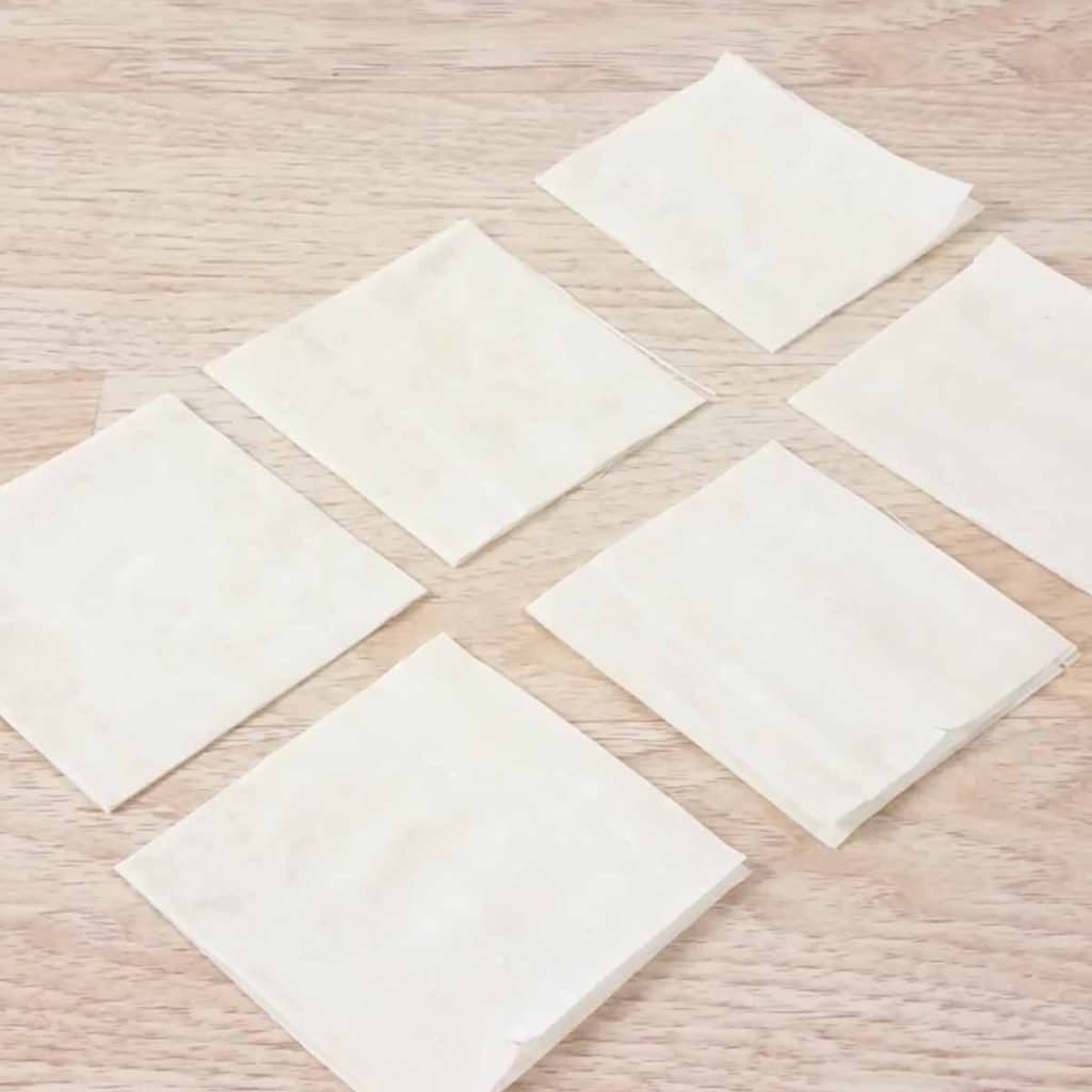 Six individual squares of phyllo dough on a wood countertop. 