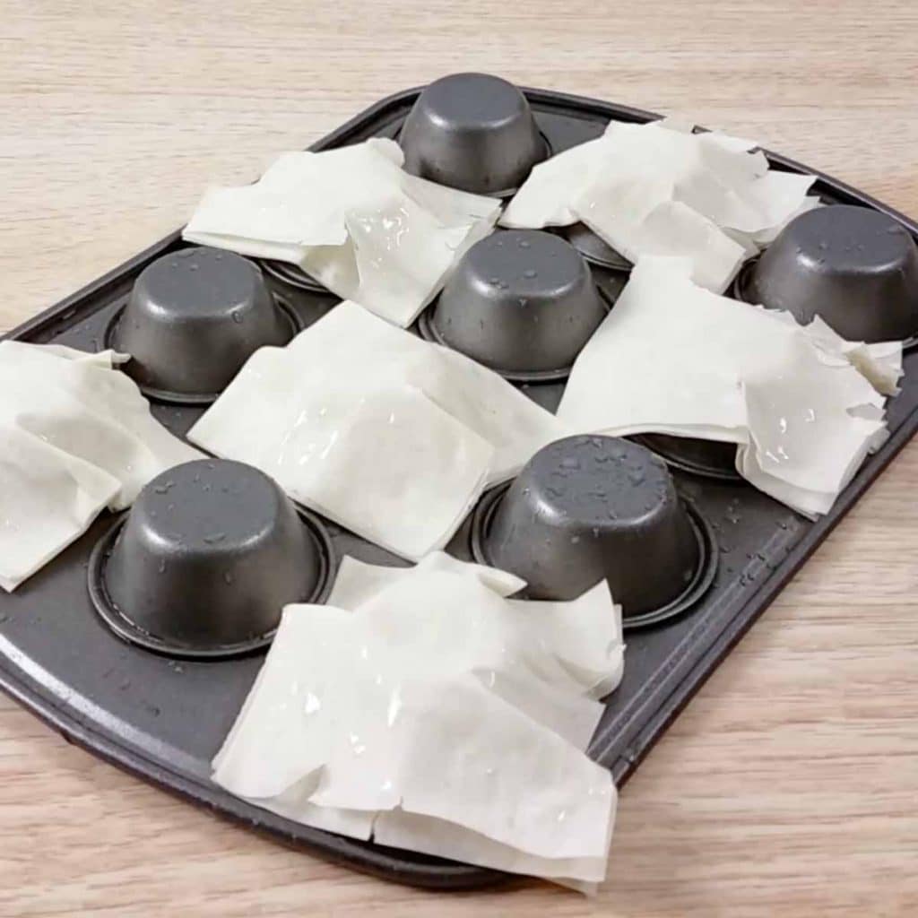Upside down cupcake tin with phyllo dough cups being molded onto the individual molds. 