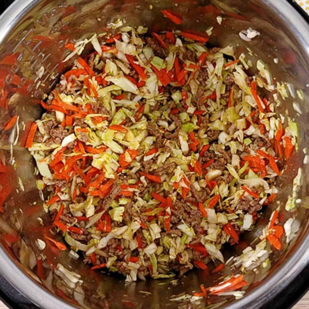 Instant Pot with cooked ingredients (cabbage, vegetables, meat, and sauce) for deconstructed egg roll cups. 