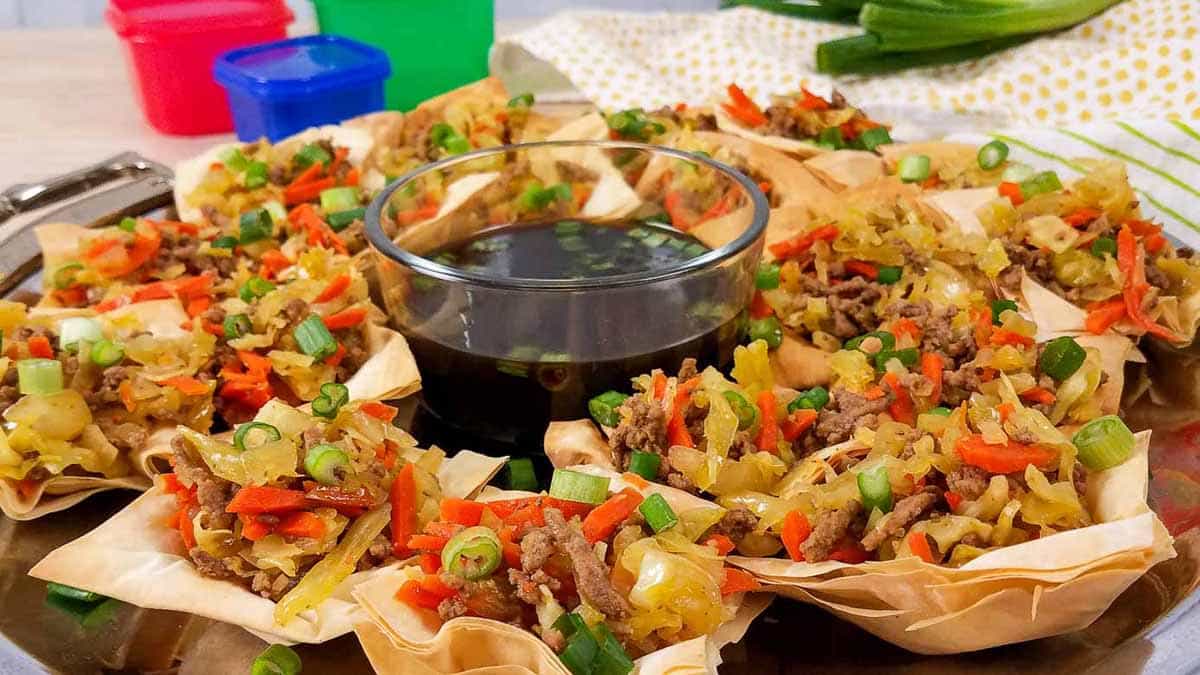 Silver tray with large circle of deconstructed egg roll cups on it, and a glass bowl of sauce in the middle.