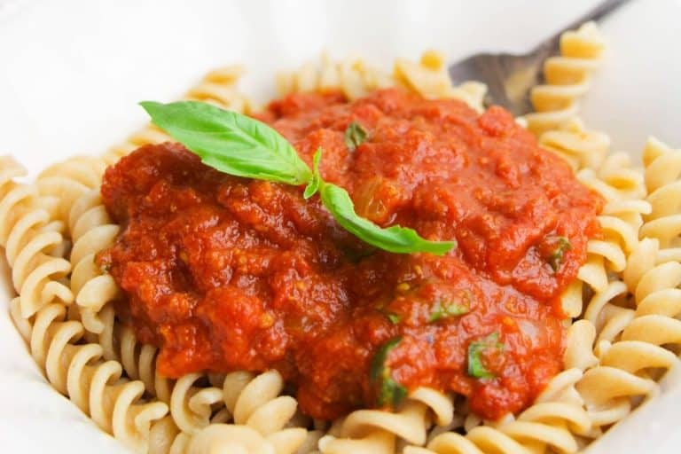 A white plate with cooked rotini pasta that has been topped with no meat spaghetti sauce and two basil leaves.