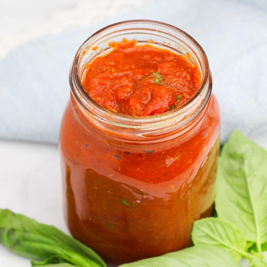 An open glass mason jar filled with homemade no meat spaghetti sauce, and a sprig of fresh basil at the base of the jar.