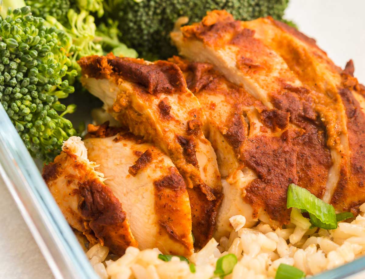 Sliced chipotle chicken next to broccoli and brown rice inside of a glass meal prep container.