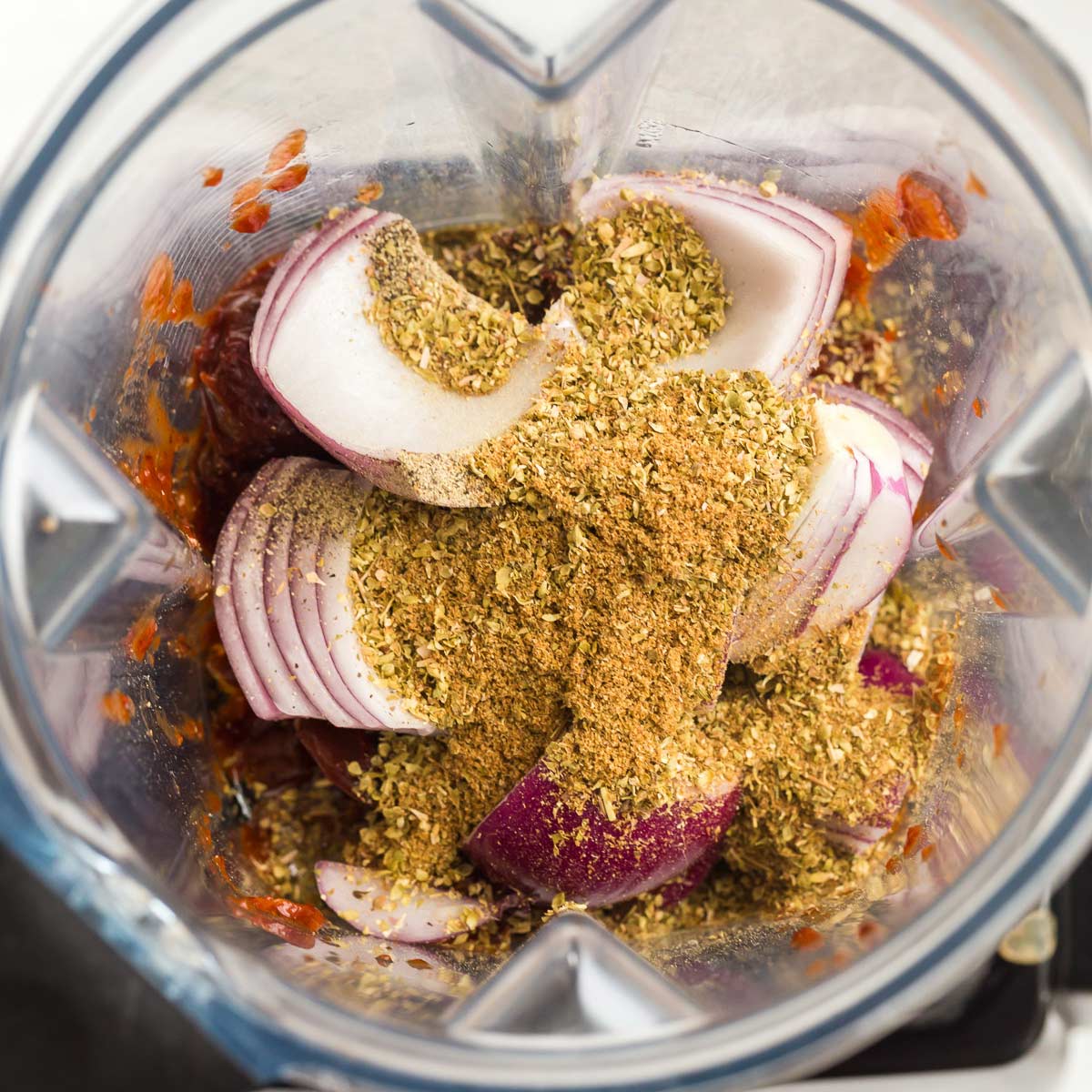 Blender with red onion, spices, and chipotle peppers before being blended.