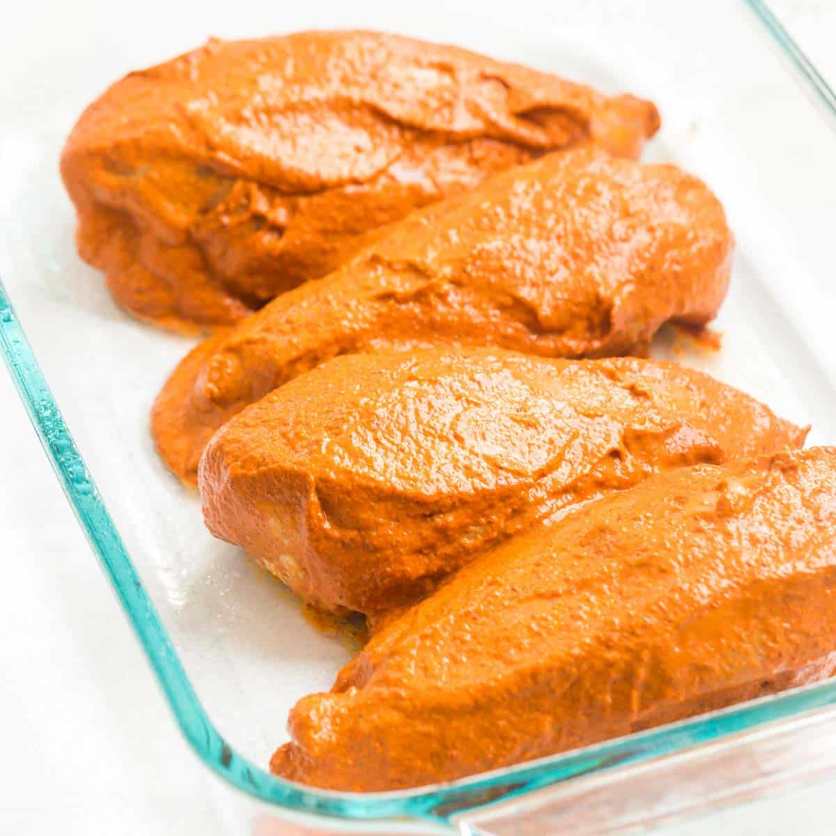 Four chipotle chicken marinated chicken breasts inside of a glass baking dish.
