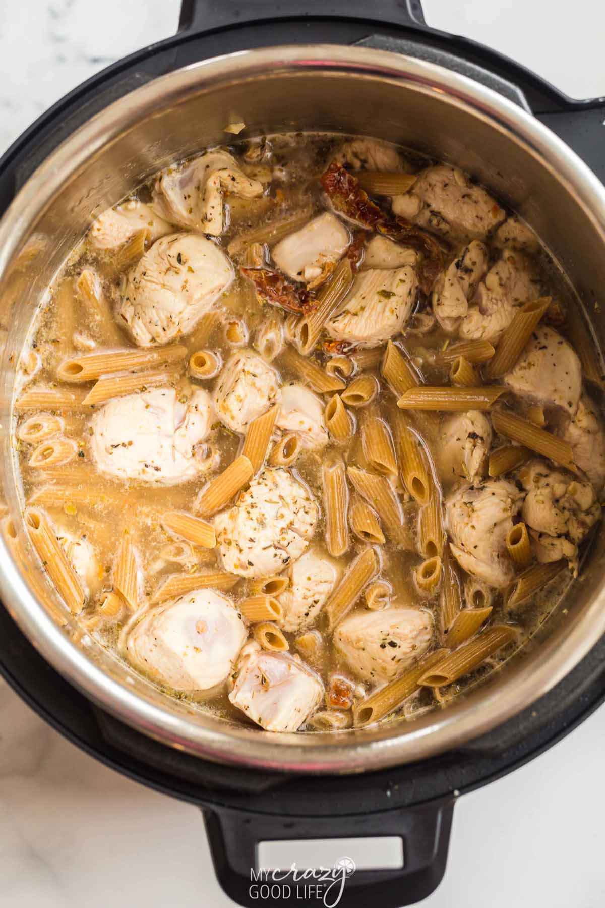 top down view of cooked ingredients in the Instant pot - chicken, pasta, broth, spices.