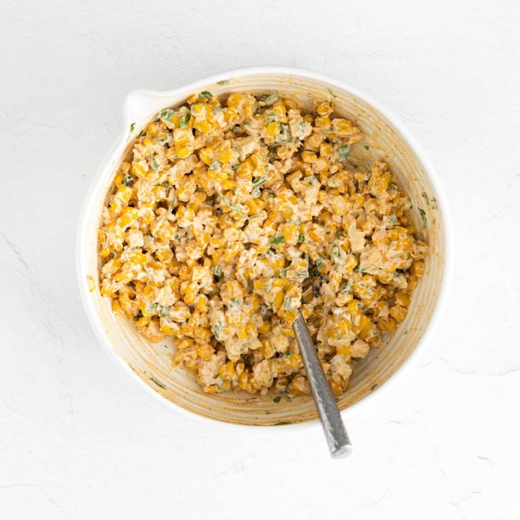 A white bowl with corn mixed together with a spicy, Mexican street corn mix.