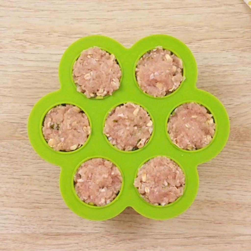 A green instant pot egg bite mold with 7 compartments full of teriyaki meatball mixture ready to be cooked.