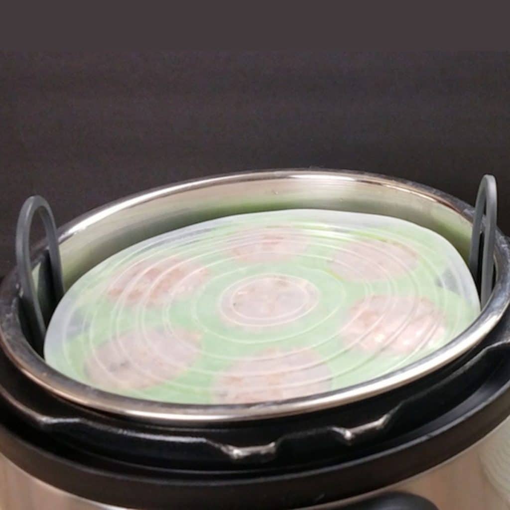 An open Instant Pot showing a covered egg bite mold that has teriyaki meatballs in it.