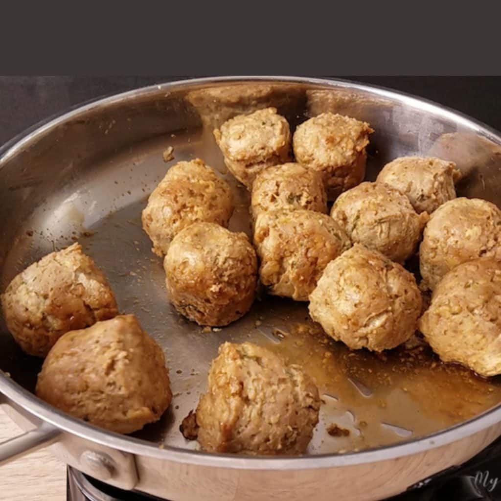 A stainless skillet with 14 teriyaki meatballs in it being coated by a teriyaki sauce.