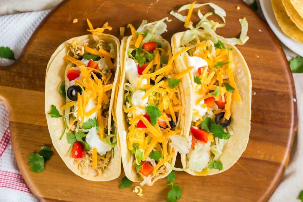 three tacos from above with chicken, tomato, cilantro, shredded cheese and sour cream