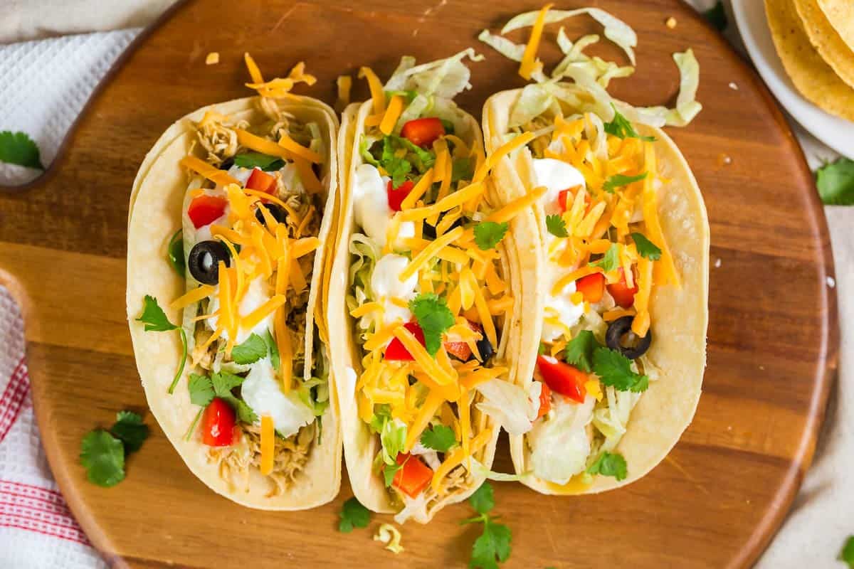 Three tacos from above with chicken, tomato, cilantro, shredded cheese and sour cream.