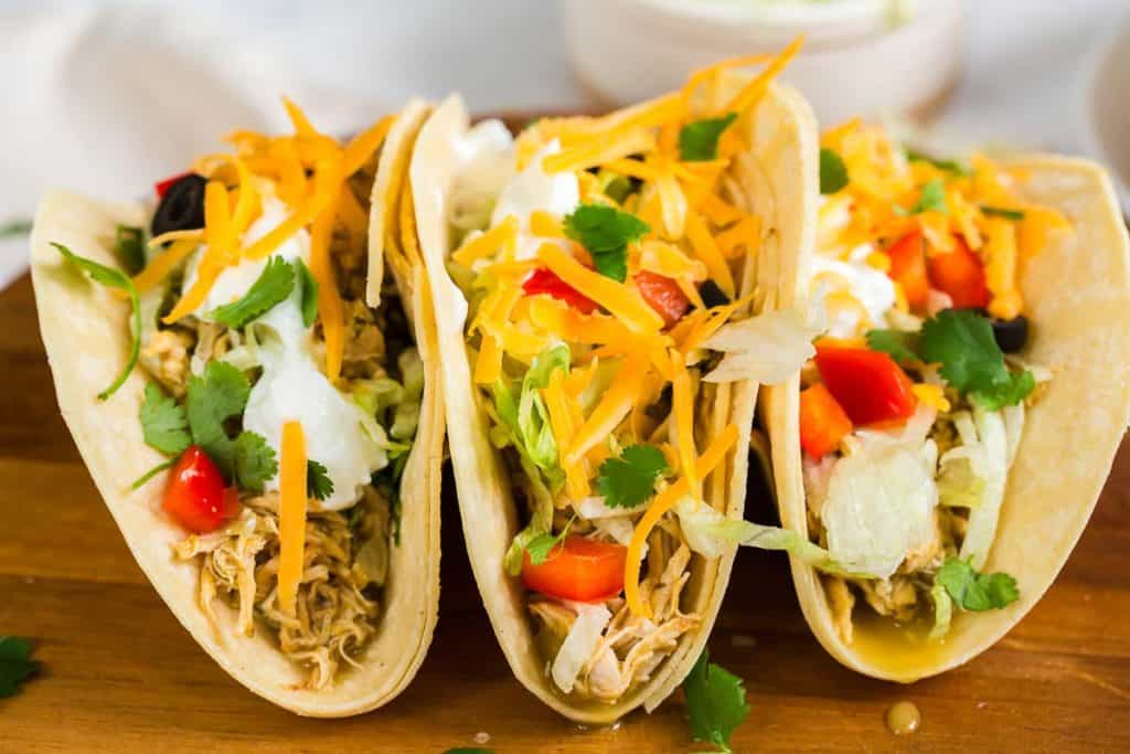 three tacos from the front with chicken, tomato, cilantro, shredded cheese and sour cream