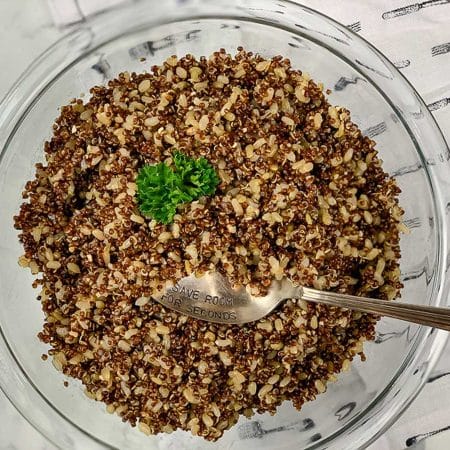 Glass bowl full of cooked red quinoa and brown rice, topped with parsley.